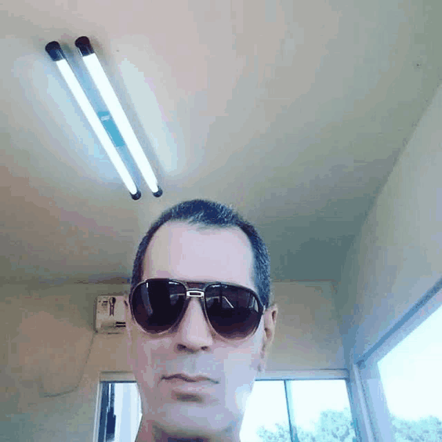 a man wearing sunglasses stands in a room with two lights on the ceiling