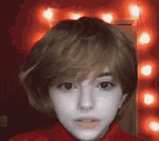 a close up of a person 's face with a red background and lights in the background .