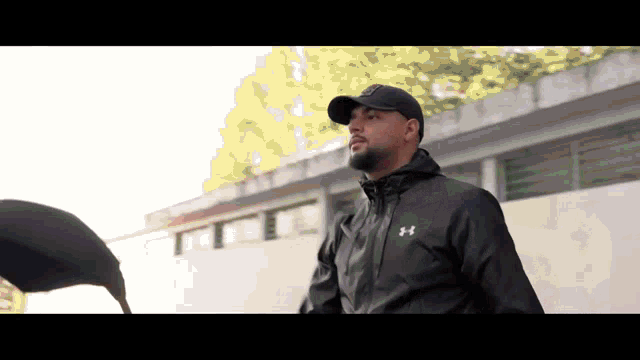 a man in a black under armour jacket stands in front of a building