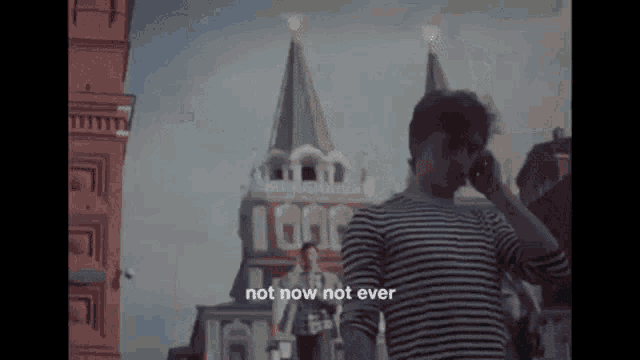 a man in a striped shirt is talking on a cell phone in front of a tower .