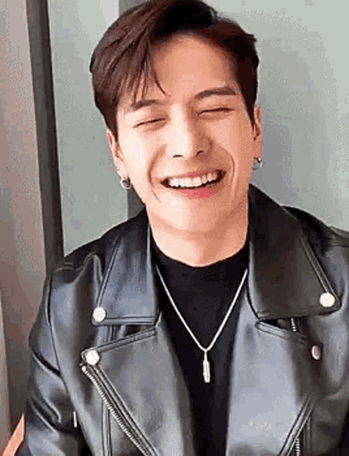 a young man wearing a black leather jacket and a necklace is smiling .
