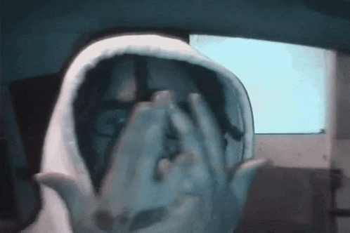 a person in a hooded sweatshirt covering their face with their hands