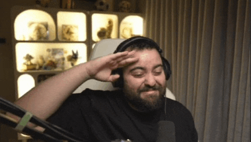 a man with a beard wearing headphones salutes in front of a microphone .