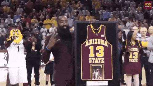 a man holds up a arizona state jersey in front of a crowd