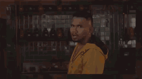 a man in a yellow hoodie is standing in front of a bar with the words `` iyaaah '' written on the screen .