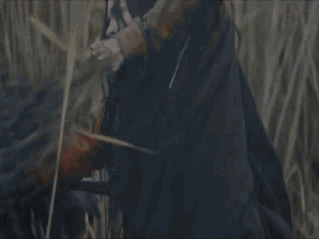a man with long hair is kneeling down in a field of tall grass .