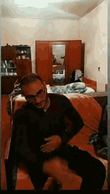 a man wearing glasses is sitting on a couch in a bedroom .