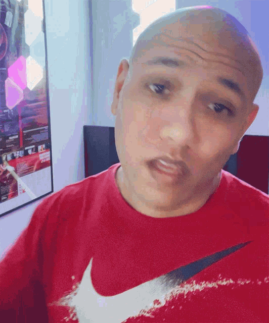 a bald man wearing a red nike shirt is making a face