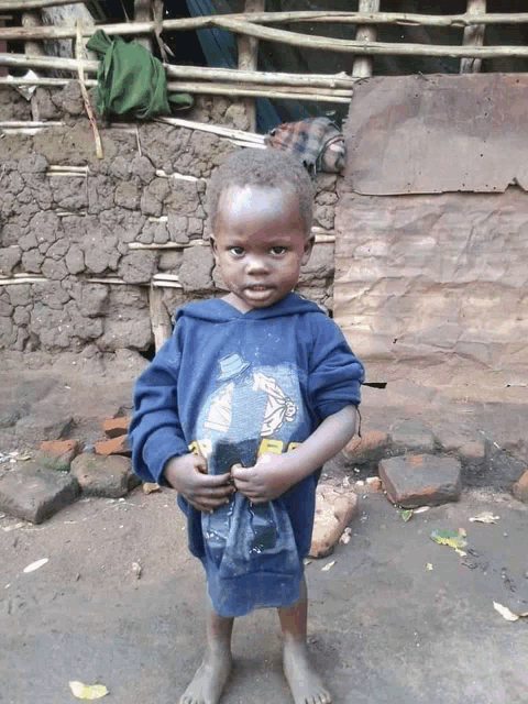 a young boy wearing a blue shirt with a picture of a man on it stands in front of a stone wall