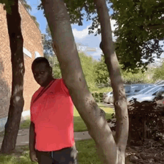 a man in a red shirt leaning against a tree trunk .