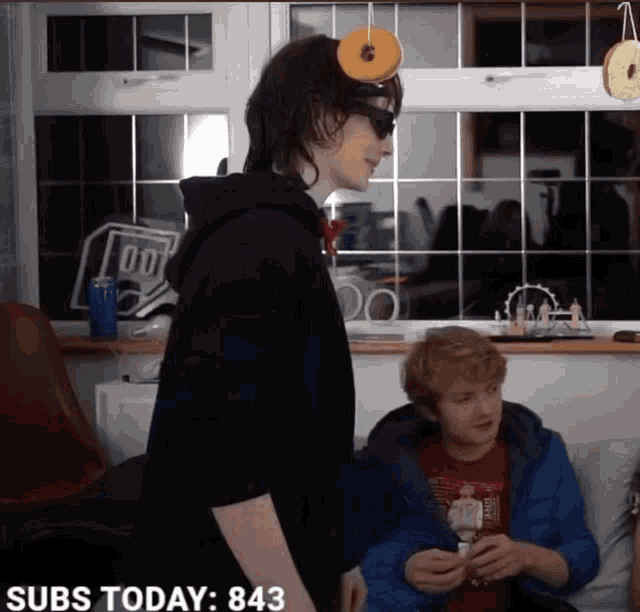 a man wearing sunglasses and a donut on his head is standing in front of a sign that says subs today