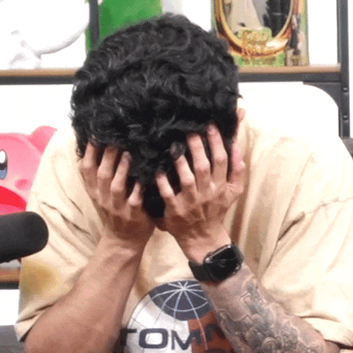 a man covering his face with his hands and a shirt that says tom