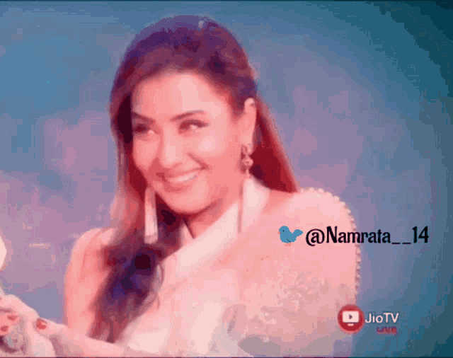 a woman in a white dress is smiling in front of a blue background with a jio tv logo in the corner