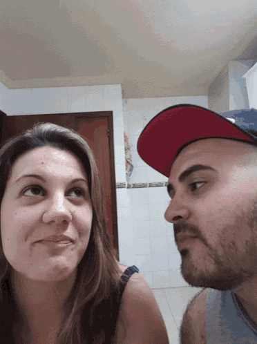 a man and a woman are looking at each other and the man is wearing a red hat