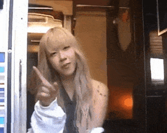 a woman with blonde hair is pointing at the camera while standing in a room .