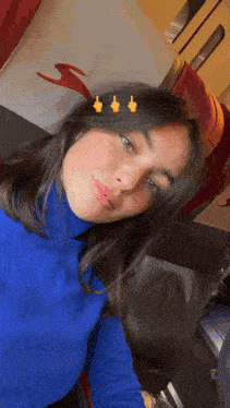 a woman wearing a blue turtleneck looks at the camera with three yellow thumbs up on her hair