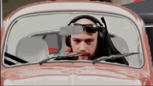 a bald man wearing sunglasses and headphones is driving a red car