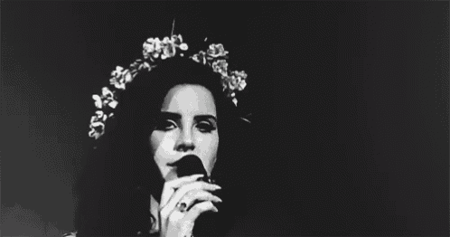 a black and white photo of a woman with a flower crown on her head sticking her tongue out .