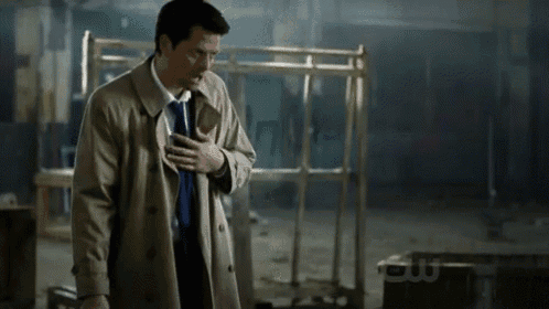 a man in a trench coat is holding his chest and says i dont know what my feelings are doing
