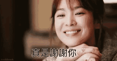 a woman is smiling with her hands folded in front of her face in a close up .