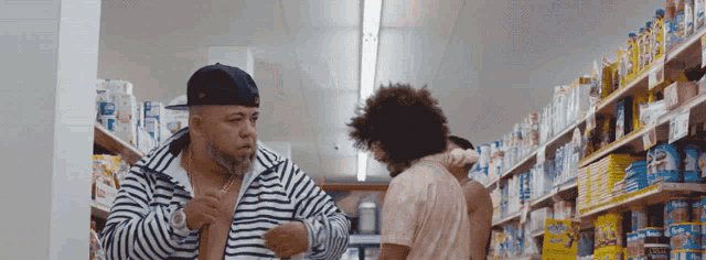a man in a striped jacket is standing in a grocery store talking to another man
