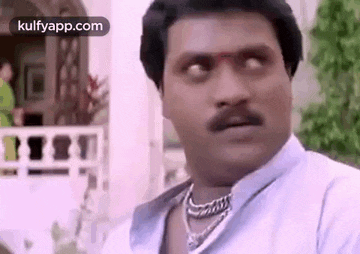 a man with a mustache is wearing a necklace and making a funny face .