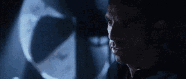 a close up of a man 's face in a dark room with a helmet in the background .
