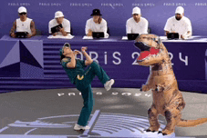 a man in a t-rex costume kicks another man in front of a paris 24 sign