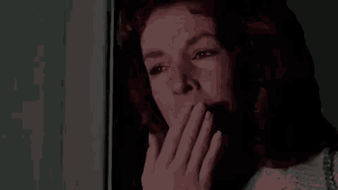 a close up of a woman covering her mouth with her hand in a dark room .