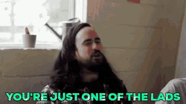 a man with long hair and a beard is sitting in front of a window .