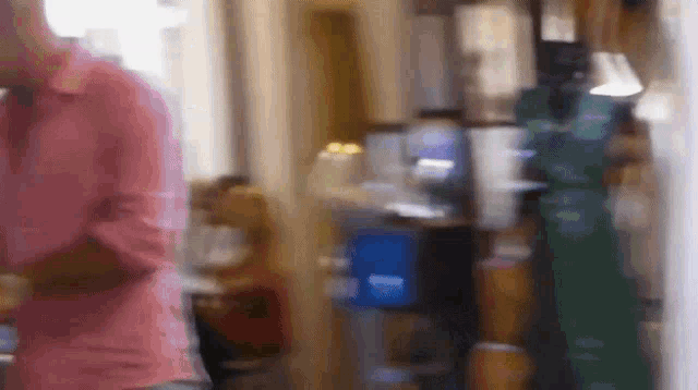 a blurry picture of a man in a pink shirt talking on a cell phone in a room .
