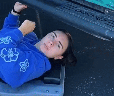 a woman in a blue sweatshirt is laying on a bench with her arms outstretched .
