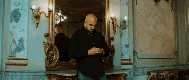 a bald man in a black shirt is standing in front of a mirror