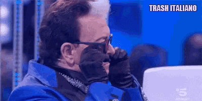 a man in a blue suit and sunglasses is covering his face with his hand .