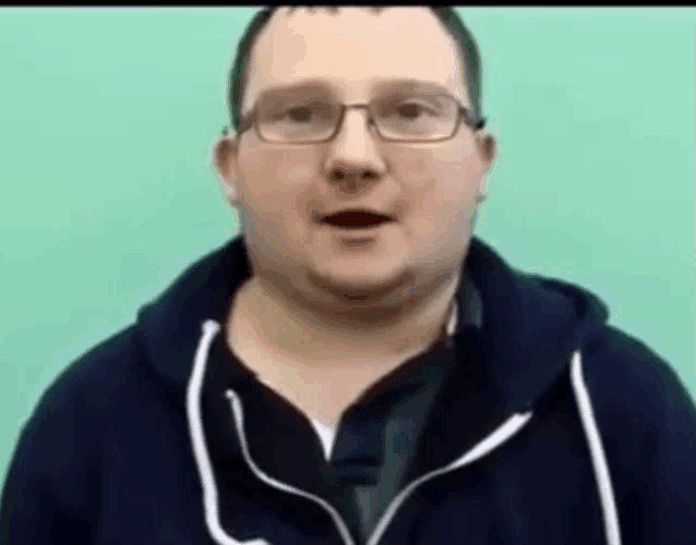 a man wearing glasses and a black hoodie is talking to the camera .