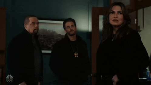 a woman in a black coat stands between two men in black jackets