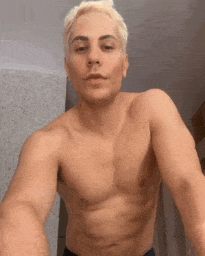 a shirtless man with blonde hair is taking a selfie in front of a mirror