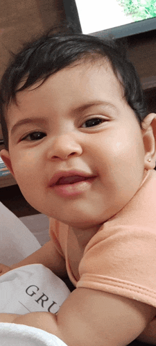 a baby in a pink shirt is smiling and looking at the camera