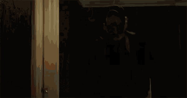 a man with a beard and hat is standing in a hallway in a dark room .