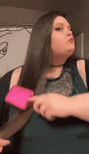 a woman in a green top is brushing her hair with a pink brush