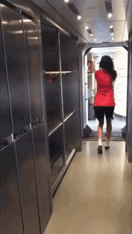 a woman in a red shirt and black shorts is walking through a hallway