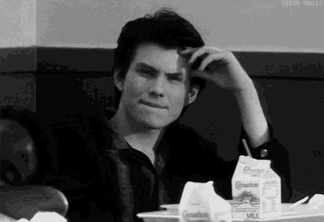 a black and white photo of a man sitting at a table with a bottle of milk and a carton of milk .