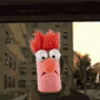 a stuffed animal with a red head and orange beak is looking out a window