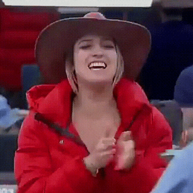 a woman wearing a cowboy hat and a red jacket is smiling and clapping .