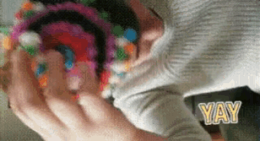 a close up of a person holding a colorful object with the word yay in the corner