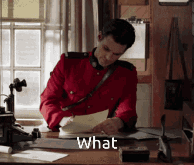 a man in a red uniform is sitting at a desk with the word what written on it