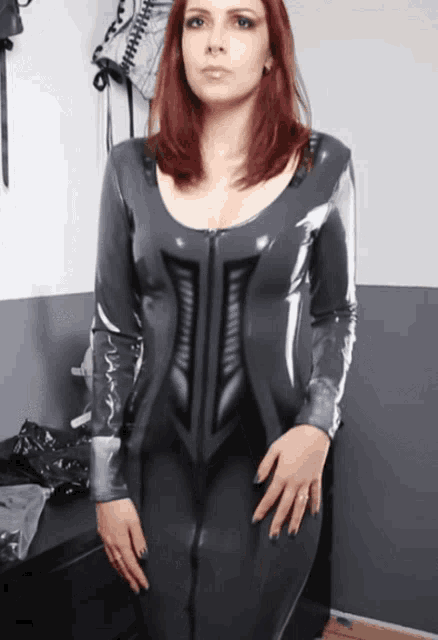 a woman in a gray latex outfit stands in front of a table