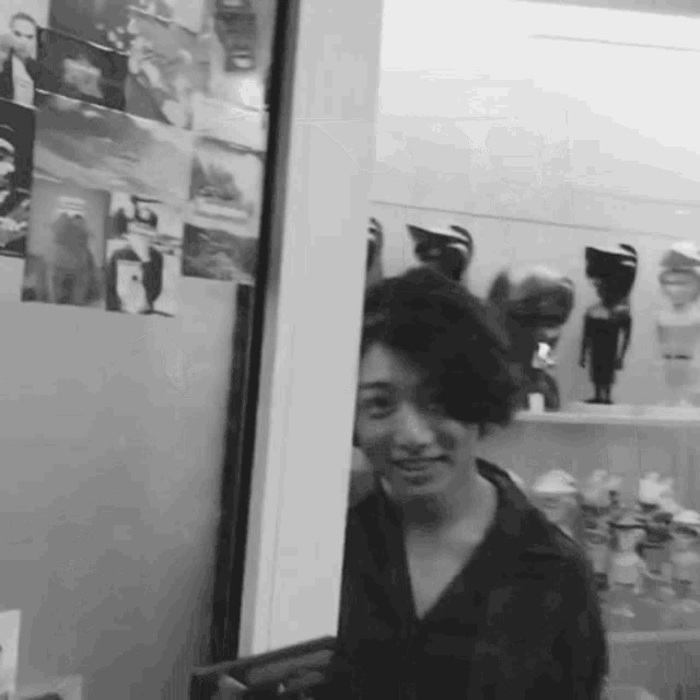a black and white photo of a woman standing in front of a wall of pictures
