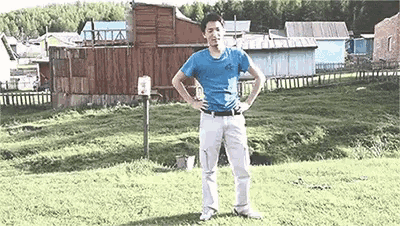 a man in a blue shirt is standing in a grassy field with his hands on his hips .