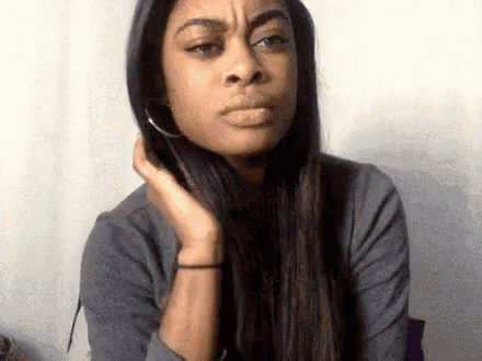 a woman with long hair and hoop earrings is making a funny face while touching her hair .